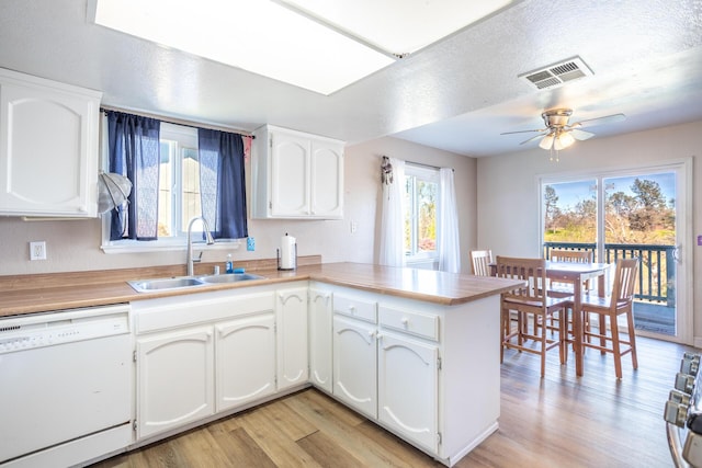 kitchen featuring light wood finished floors, visible vents, a peninsula, white dishwasher, and a sink