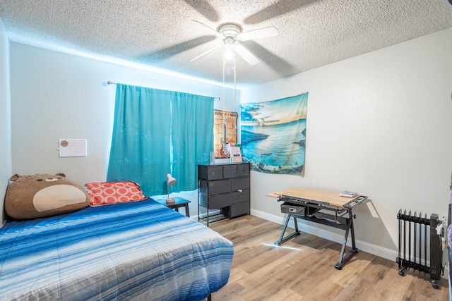 bedroom featuring wood finished floors, baseboards, radiator heating unit, ceiling fan, and a textured ceiling