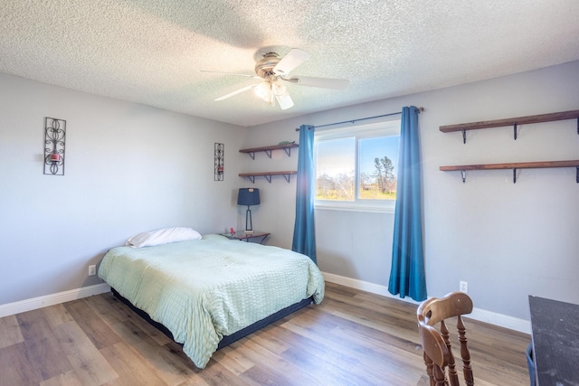 bedroom with ceiling fan, a textured ceiling, baseboards, and wood finished floors