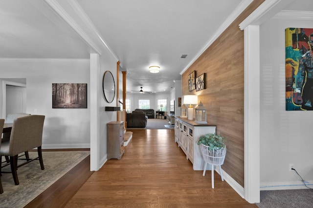 corridor with baseboards, wood finished floors, visible vents, and ornamental molding