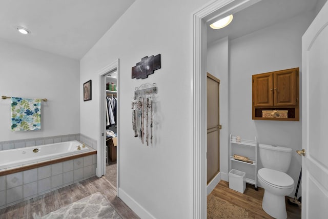 full bath featuring wood finished floors, baseboards, a walk in closet, a garden tub, and toilet