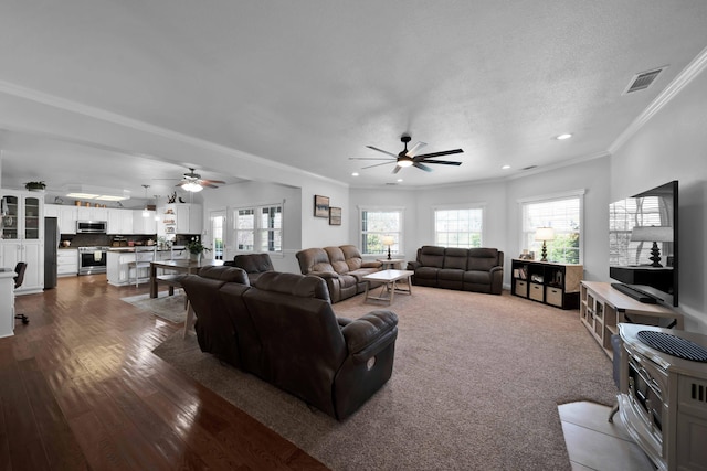 living room with dark wood finished floors, visible vents, crown molding, and ceiling fan