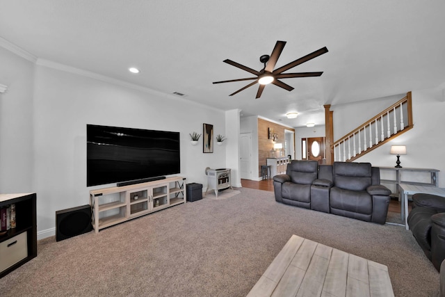 carpeted living room with baseboards, a wood stove, ceiling fan, stairs, and crown molding