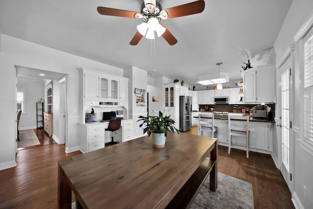 dining space featuring a ceiling fan, baseboards, dark wood-type flooring, and built in desk