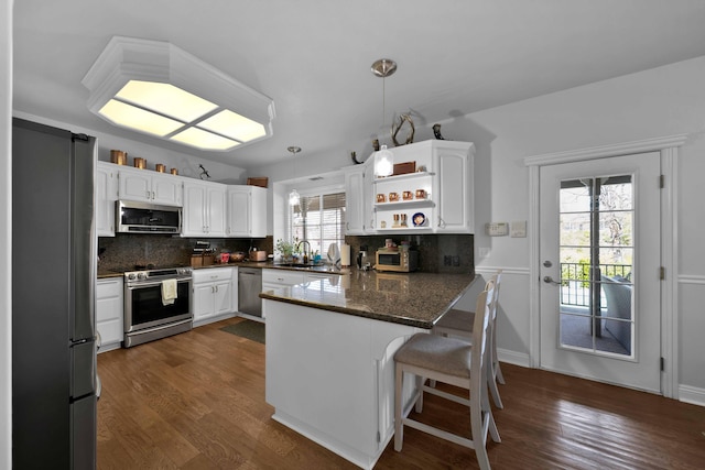 kitchen featuring a peninsula, open shelves, a sink, appliances with stainless steel finishes, and backsplash