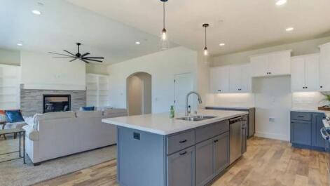 kitchen with a kitchen island with sink, arched walkways, ceiling fan, a sink, and white cabinetry