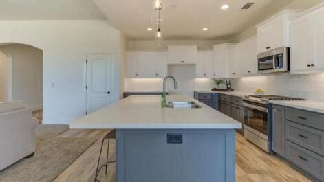 kitchen with a center island with sink, a sink, stainless steel appliances, arched walkways, and light countertops