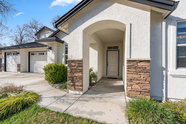 view of exterior entry featuring stone siding, stucco siding, an attached garage, and concrete driveway