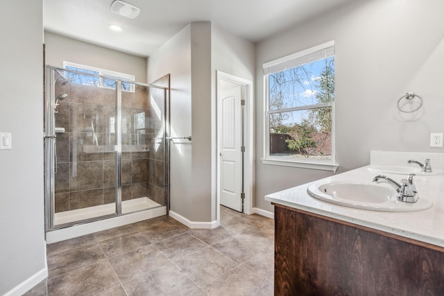 bathroom featuring double vanity, a shower stall, baseboards, and a sink