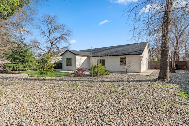 rear view of house with stucco siding, a patio area, and fence