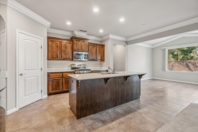 kitchen featuring stainless steel microwave, a center island with sink, gas range, a breakfast bar area, and a sink