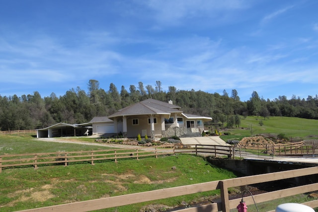 view of front of house with fence, a wooded view, a front yard, and a carport