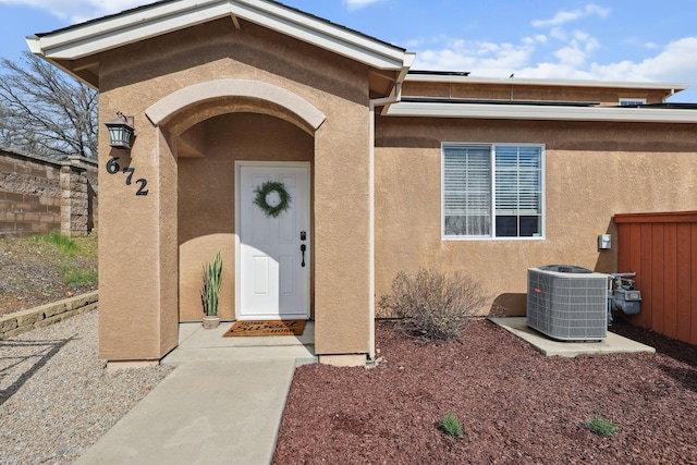 doorway to property with roof mounted solar panels, central AC unit, fence, and stucco siding