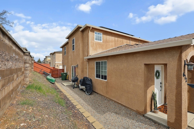 back of property with solar panels, fence, and stucco siding