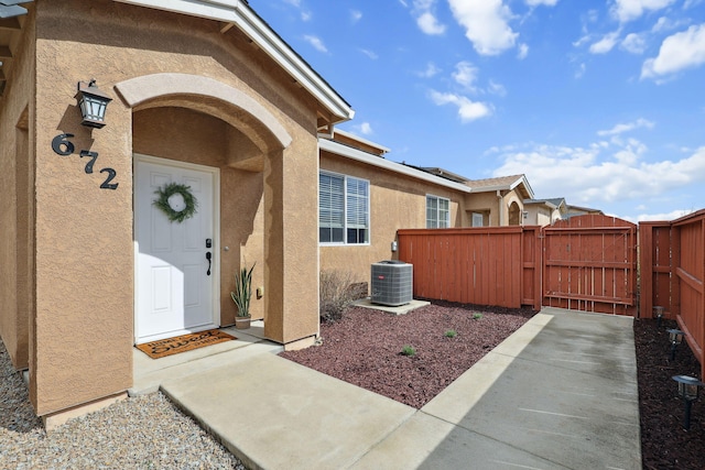 view of exterior entry with central air condition unit, stucco siding, fence, and a gate