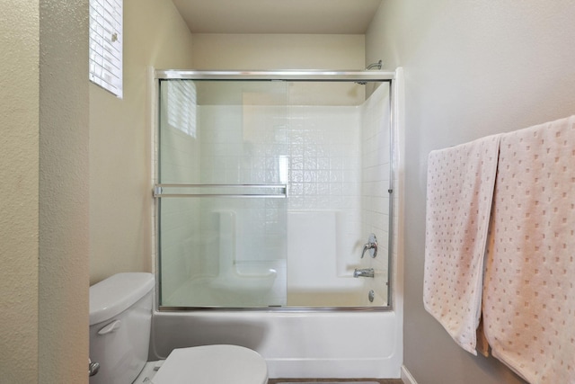 full bath with toilet and shower / bath combination with glass door