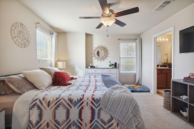 carpeted bedroom with visible vents, multiple windows, ensuite bathroom, and ceiling fan