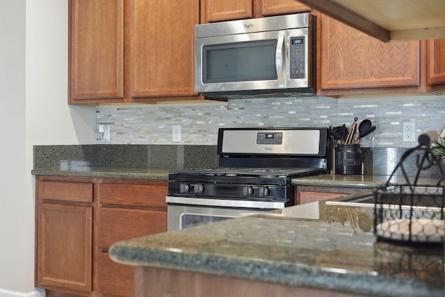 kitchen with dark stone countertops, stainless steel appliances, brown cabinets, and decorative backsplash