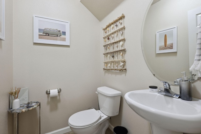 bathroom with toilet, lofted ceiling, baseboards, and a sink