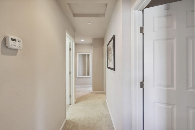 hall with baseboards, light carpet, and attic access