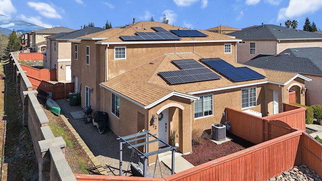 exterior space with central air condition unit, a residential view, roof mounted solar panels, stucco siding, and a fenced backyard