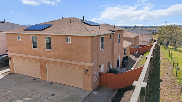 rear view of property featuring solar panels, fence, concrete driveway, stucco siding, and an attached garage