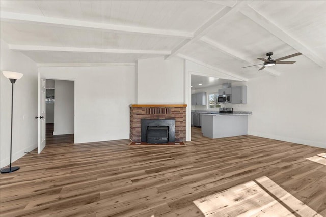 unfurnished living room featuring a ceiling fan, wood finished floors, baseboards, lofted ceiling with beams, and a fireplace