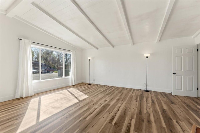 empty room featuring lofted ceiling with beams, baseboards, and wood finished floors