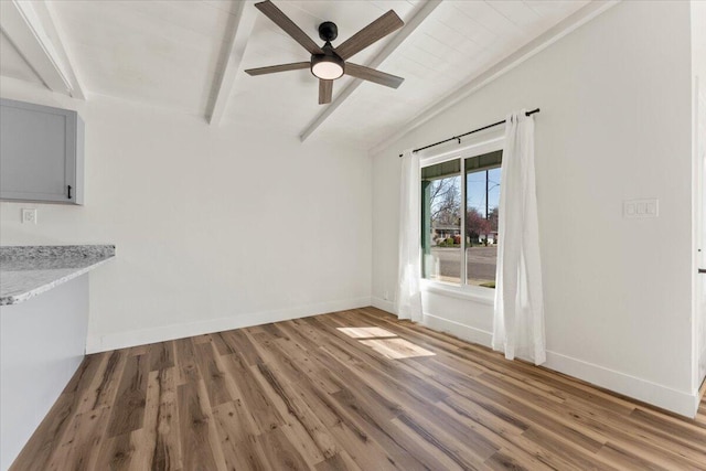 unfurnished dining area featuring lofted ceiling with beams, wood finished floors, a ceiling fan, and baseboards