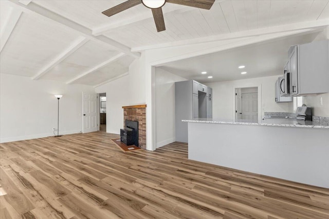 unfurnished living room with light wood-style flooring, lofted ceiling with beams, a fireplace, baseboards, and ceiling fan