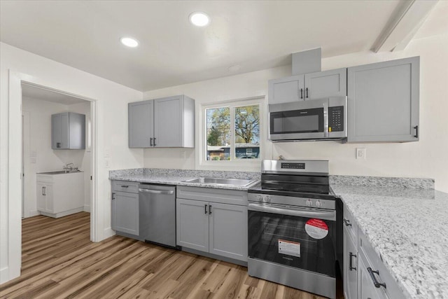 kitchen featuring light wood-style flooring, gray cabinets, appliances with stainless steel finishes, and a sink