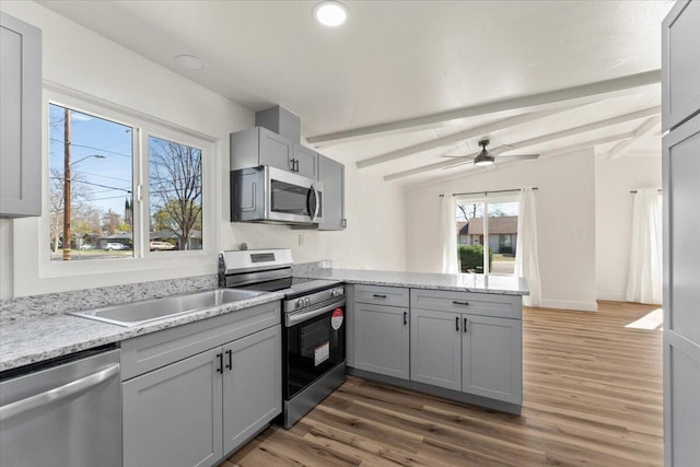 kitchen featuring lofted ceiling with beams, gray cabinets, appliances with stainless steel finishes, a peninsula, and wood finished floors