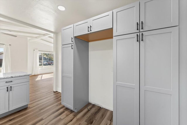 kitchen featuring vaulted ceiling with beams, light wood-style floors, and light stone countertops