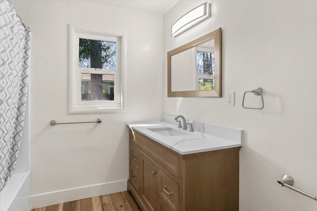 full bath with baseboards, a healthy amount of sunlight, wood finished floors, and vanity