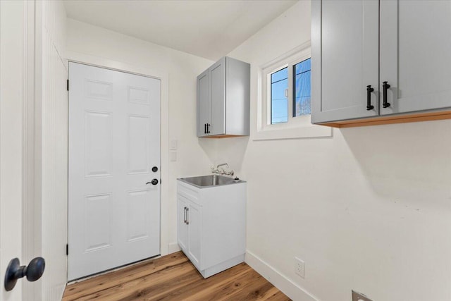 washroom featuring baseboards, light wood-type flooring, and a sink