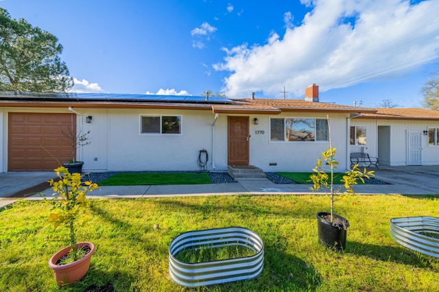 single story home featuring solar panels, an attached garage, a chimney, and a front yard