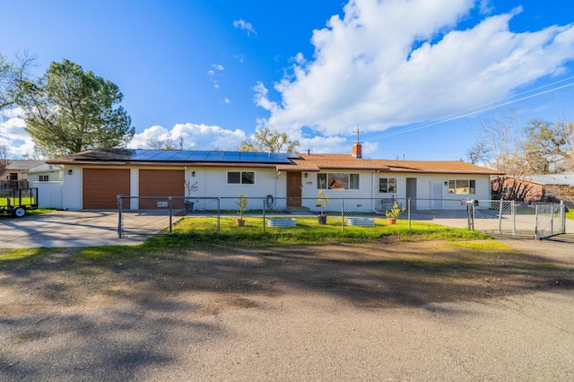 ranch-style house featuring solar panels, a fenced front yard, concrete driveway, a garage, and a gate