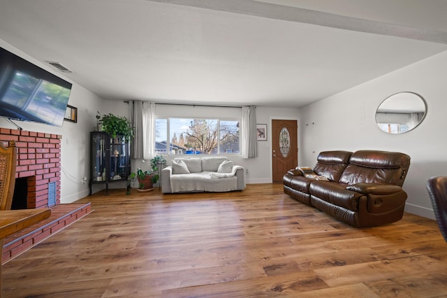 living room with visible vents, a brick fireplace, baseboards, and wood finished floors