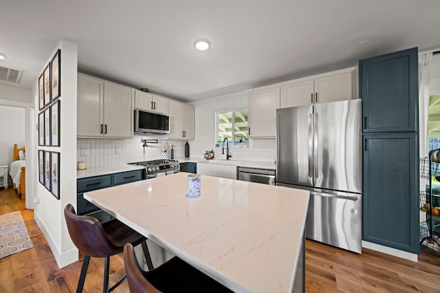 kitchen with light stone counters, wood finished floors, visible vents, stainless steel appliances, and tasteful backsplash