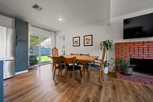 dining room featuring visible vents, a brick fireplace, and wood finished floors