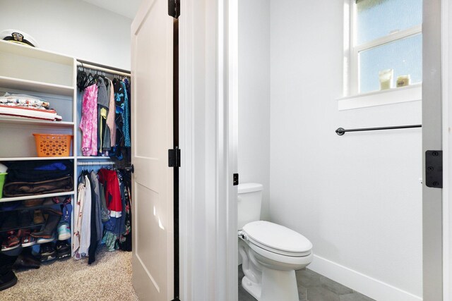 bathroom with toilet, a walk in closet, and baseboards