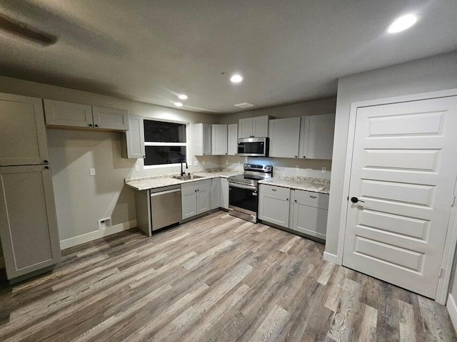 kitchen featuring light wood finished floors, gray cabinetry, baseboards, appliances with stainless steel finishes, and a sink