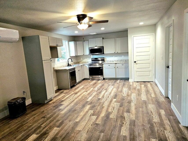 kitchen with a wall unit AC, wood finished floors, ceiling fan, a sink, and appliances with stainless steel finishes