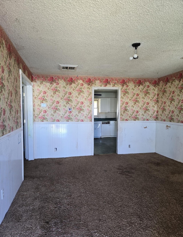 empty room with carpet, visible vents, a wainscoted wall, wallpapered walls, and a textured ceiling