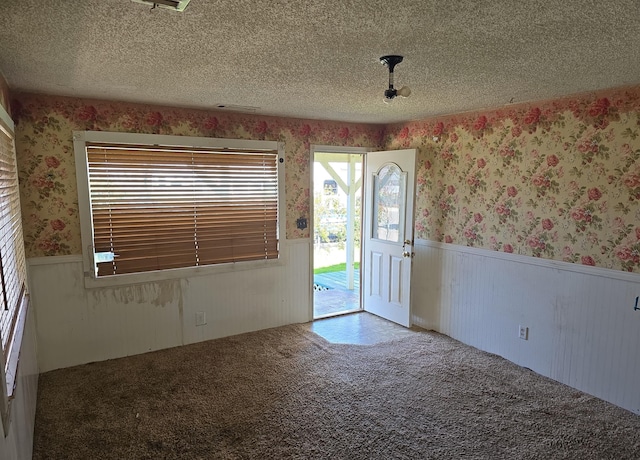 spare room featuring wallpapered walls, a textured ceiling, carpet floors, and wainscoting