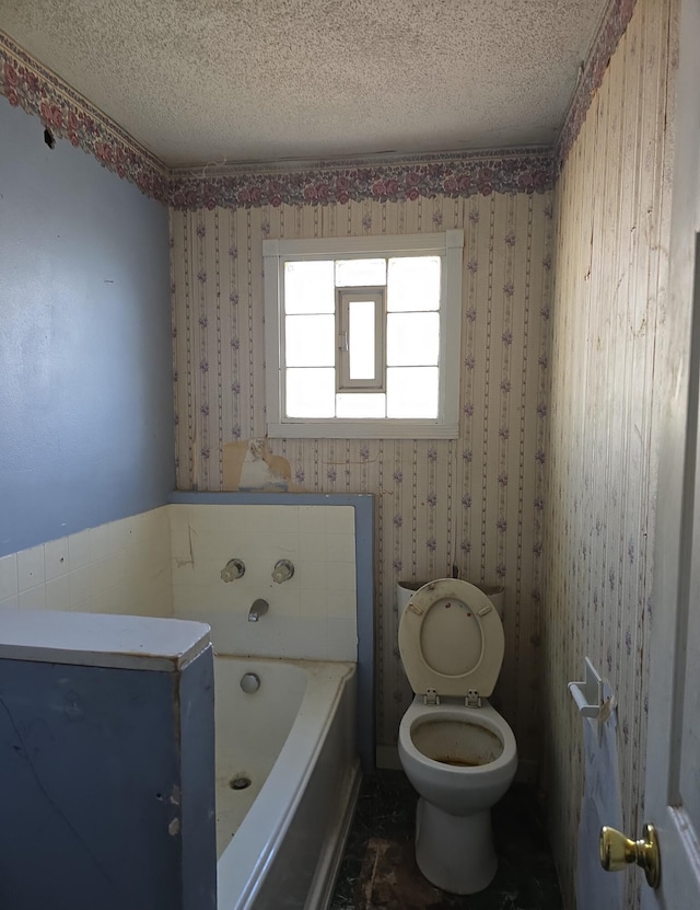 full bath with wallpapered walls, toilet, a bathtub, and a textured ceiling