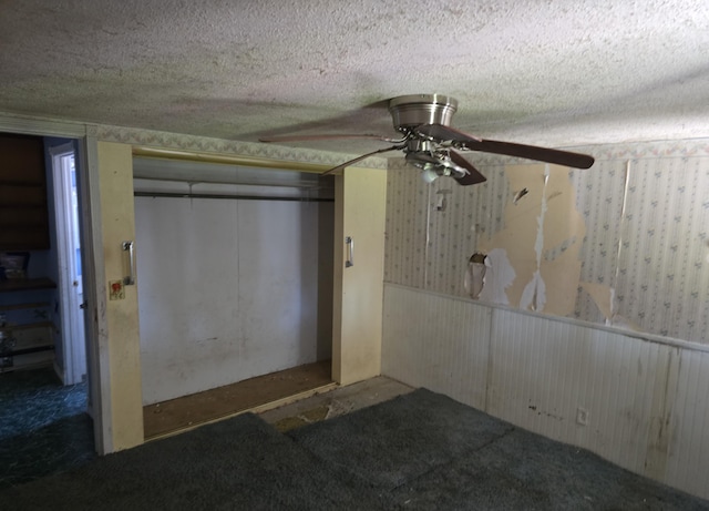 unfurnished bedroom with ceiling fan, wainscoting, a closet, and a textured ceiling