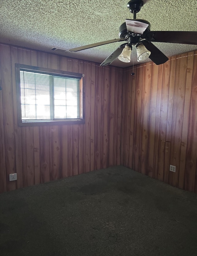 unfurnished room with a ceiling fan, wood walls, and a textured ceiling