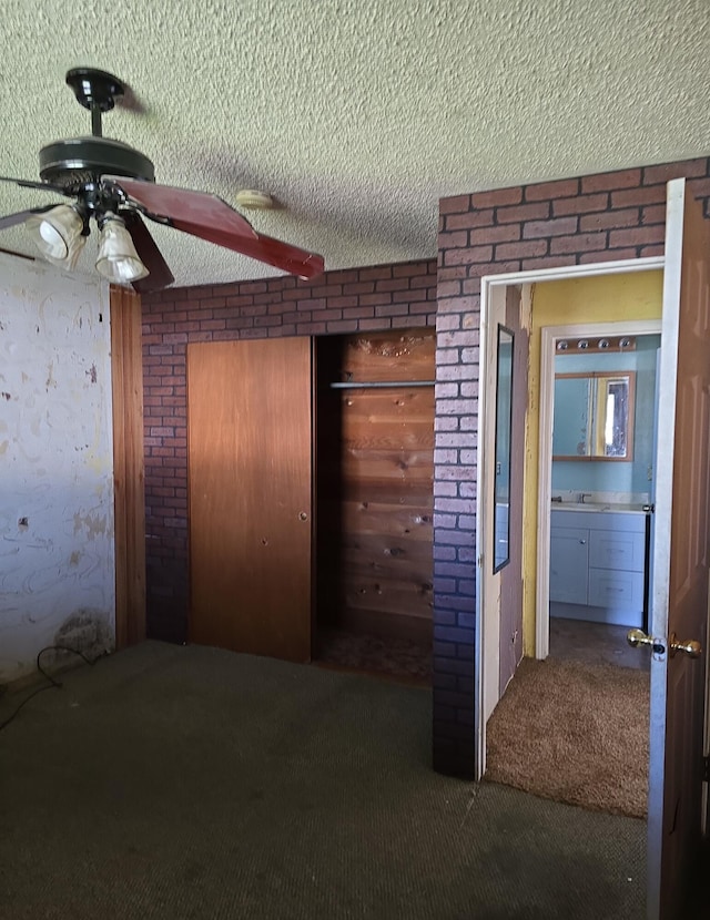 unfurnished bedroom featuring a closet, carpet floors, a textured ceiling, and brick wall