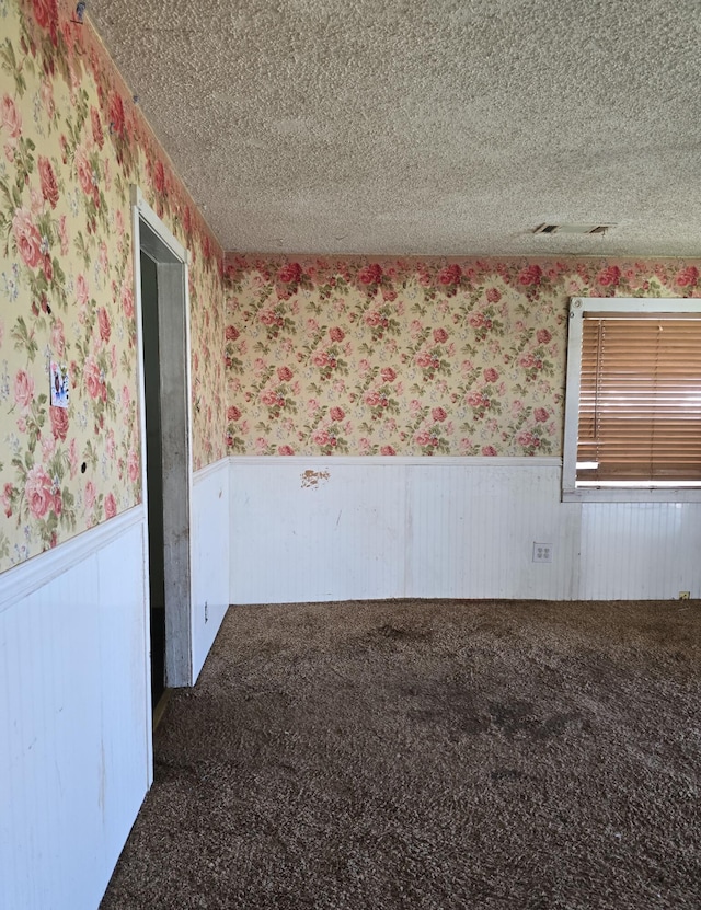 carpeted empty room with a wainscoted wall, a textured ceiling, and wallpapered walls